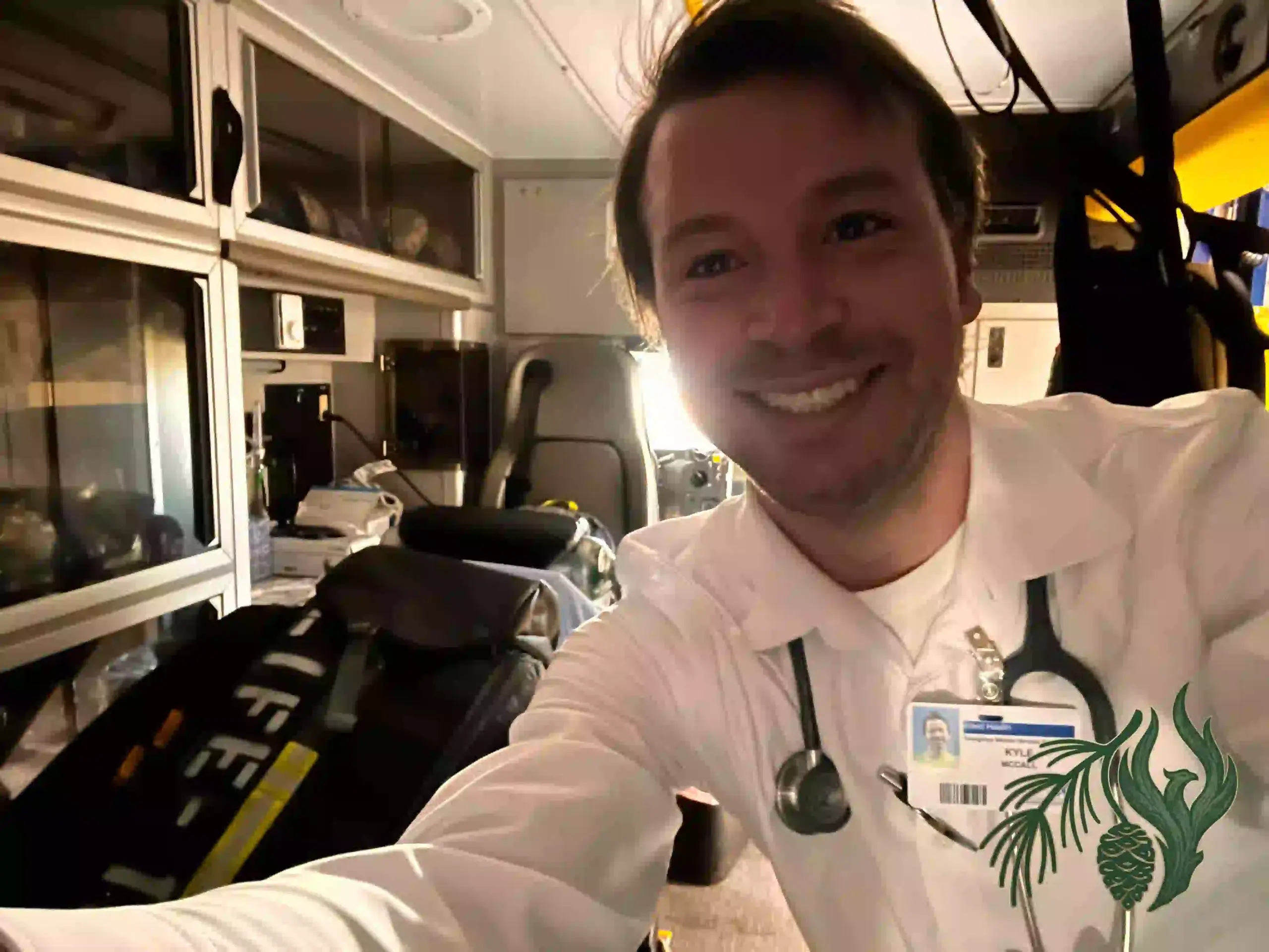 Kyle McCall, wearing a white EMS uniform and stethoscope, smiling in the back of an ambulance.