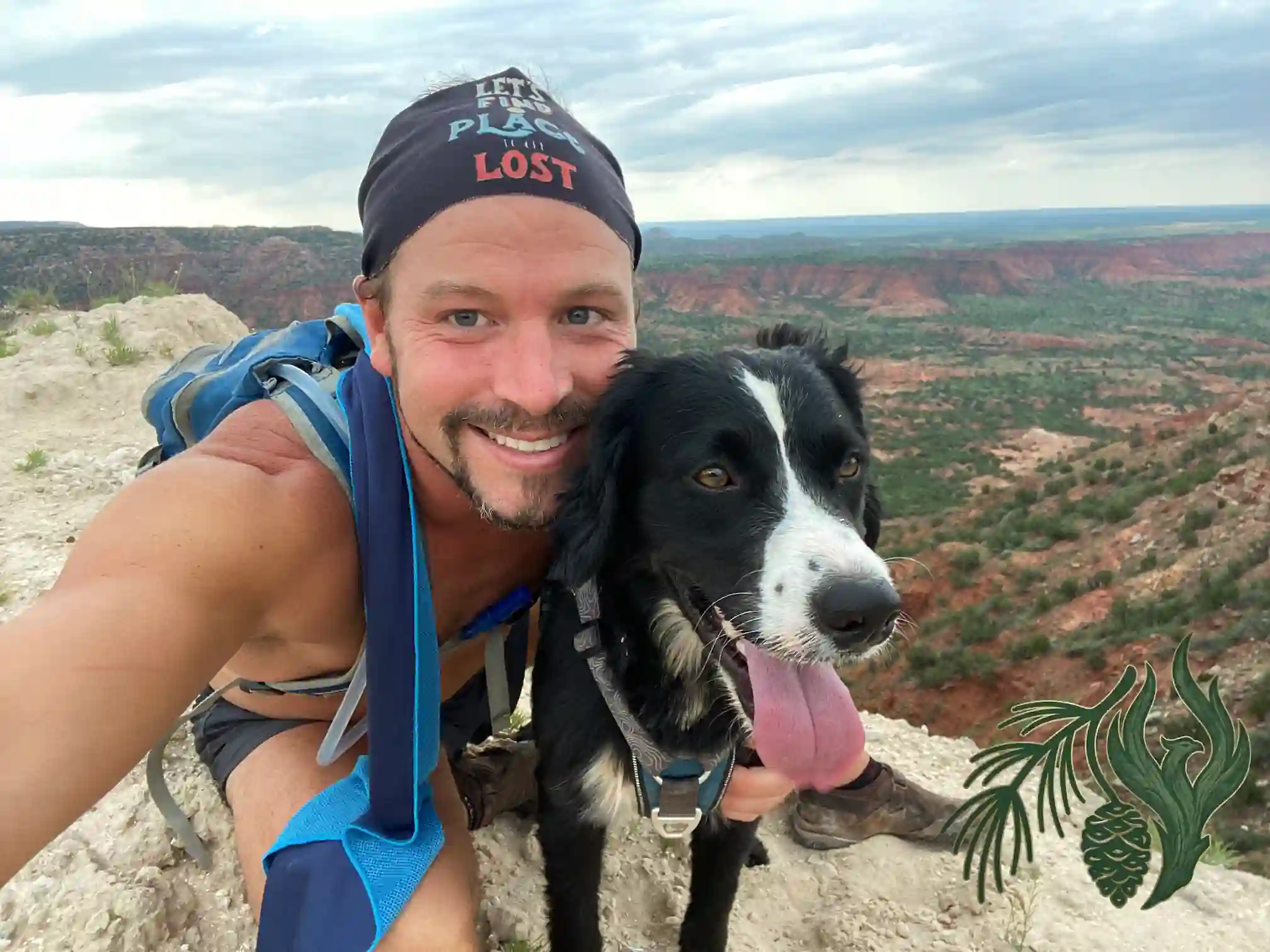 Kyle D McCall and his black-and-white service dog, Kauhlin, smiling together while hiking on a rocky ridge overlooking the beautiful Caprock Canyons of Texas.