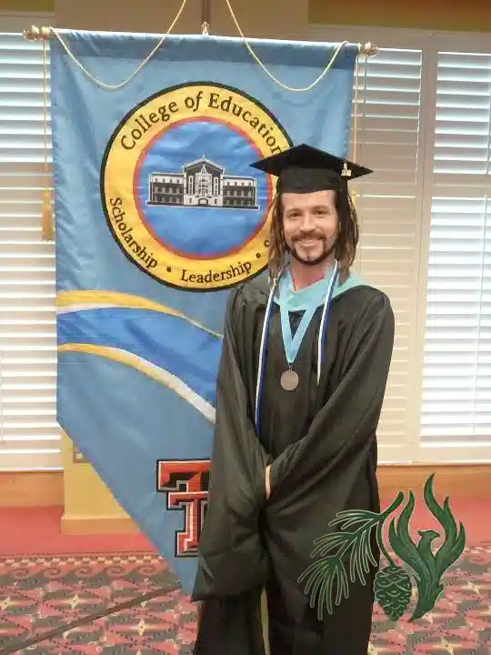 Kyle McCall wearing a graduation gown and cap, standing proudly in front of a Texas Tech College of Education banner.